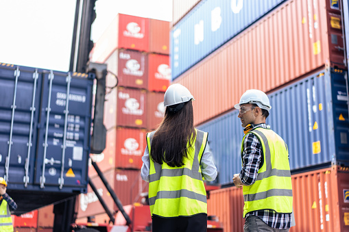 Two people stand in front of a container terminal.