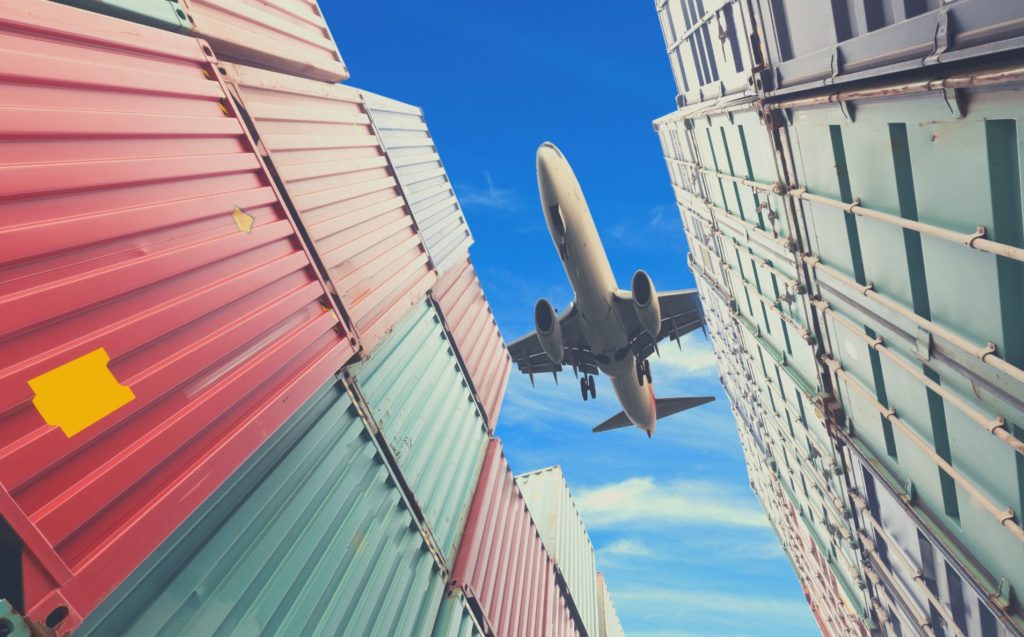 Plane flies over piled containers.