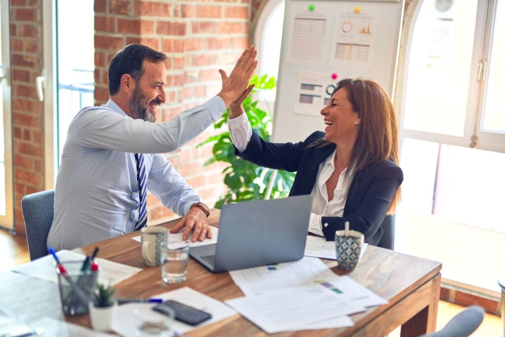 Woman and man in an office in front of a laptop, high-fiving each other.