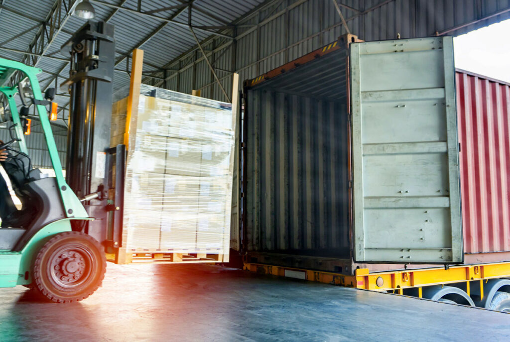 Gabelstaplerfahrer beim Entladen einer Palette mit Versandprodukten in einen Container.