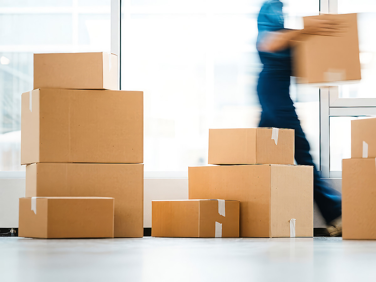 Paketversand Geschäftskunden: Pakestapel mit einem Mann, der ein Paket trägt.