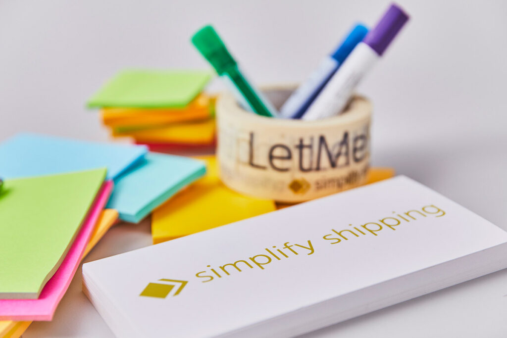 Sobre la mesa hay blocs de notas con el eslogan de LetMeShip: «simplifica los envíos».