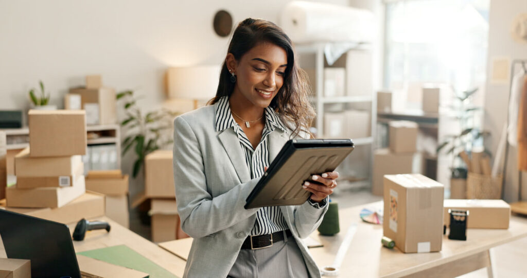 Woman smiling, with tablet in an office full of parcels