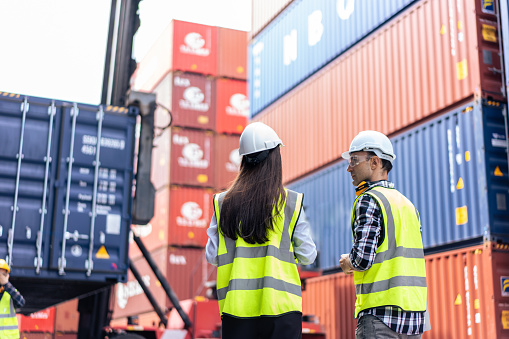 Hombres y mujeres caucásicos trabajando en una terminal de contenedores. Atractivos ingenieros procesan pedidos y productos en el almacén logístico de un buque de carga para la importación y exportación en el puerto.