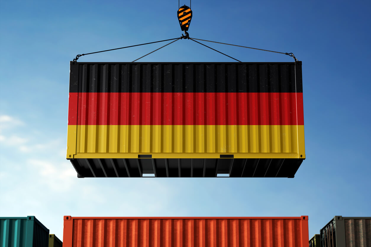 Importación de Alemania: Contenedores con bandera alemana en una grúa bajo un cielo azul.