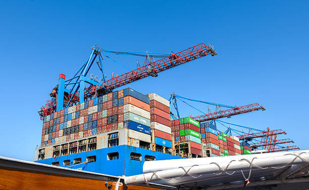 Seefracht im Nahost-Konflikt: Schiff mit Containern und Ladekränen vor blauem Himmel im Hafen.