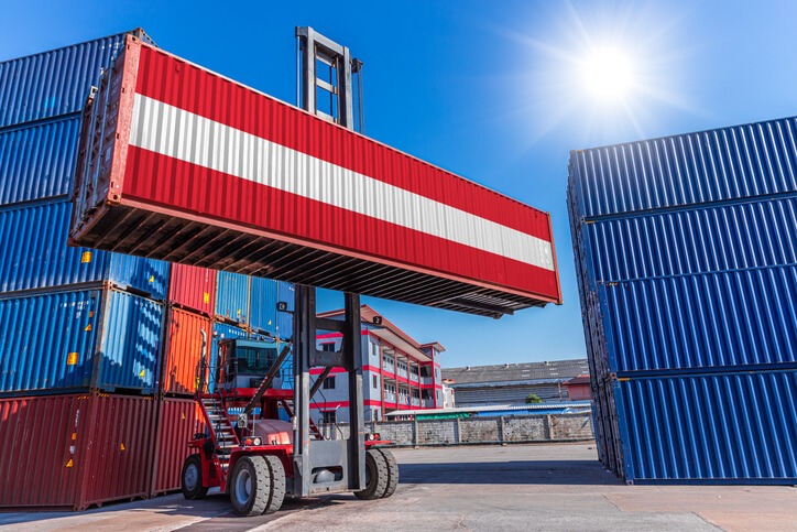 Versand von Deutschland nach Österreich. Bild zeigt einen Stacker in einem Containerterminal, der einen Container mit der österreichischen Flagge transportiert.